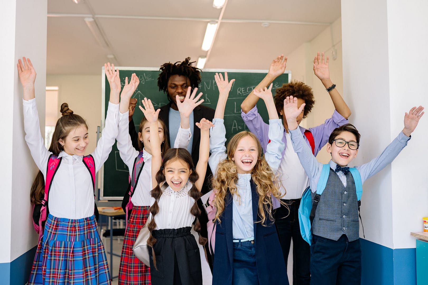 Pupils in school uniform raising their hands in class